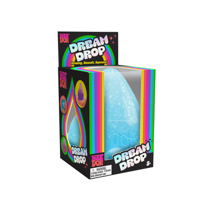 A Dream Drop in its packaging. The packaging is primarily black with rainbow-colored accents and text that reads "Dream Drop" and "". The toy inside is a blue, drop-shaped, squeezable item. Suitable for ages 3 and up.