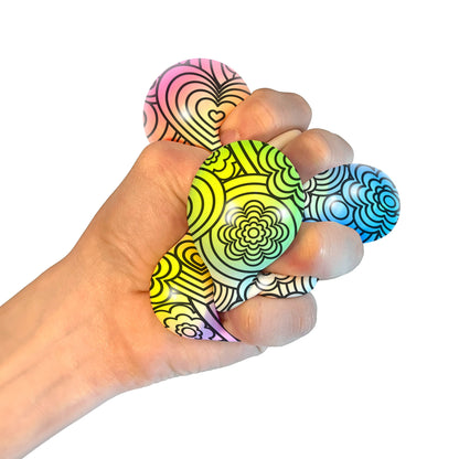 A hand squeezing a Press-Doh. The colorful doh is visible through the white and black designs of the exterior.