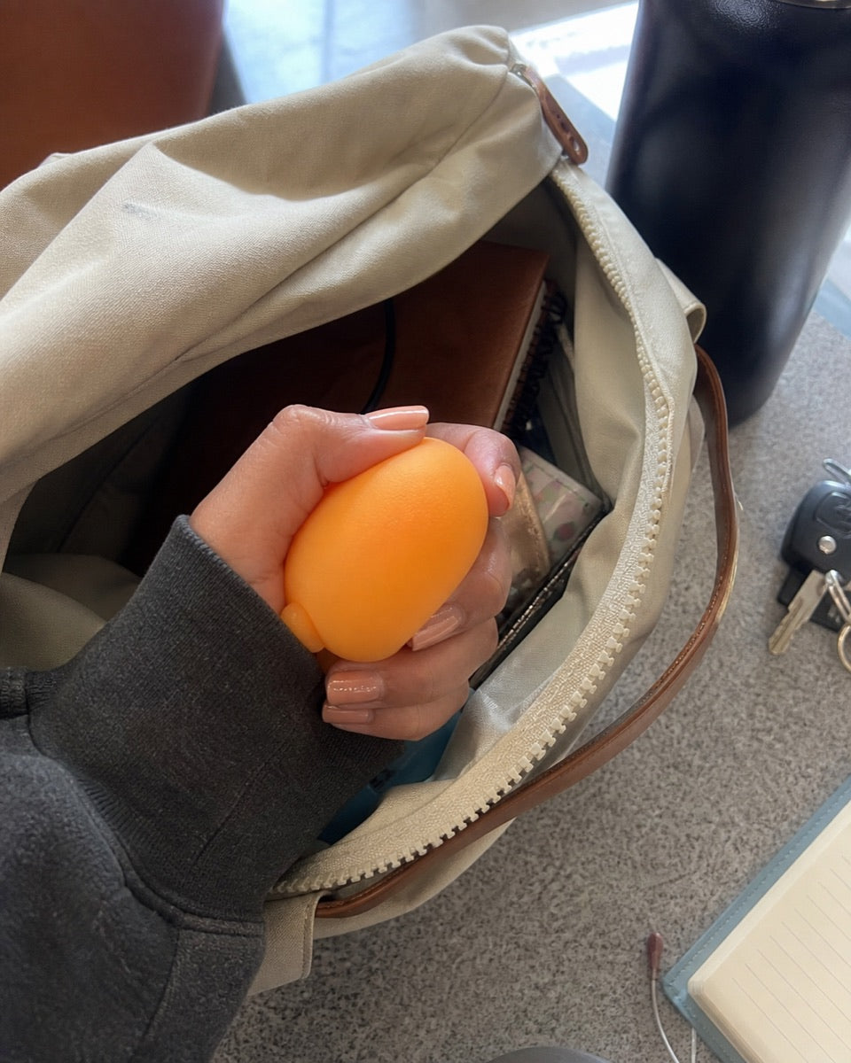 A hand holding an orange squishy toy near an open bag