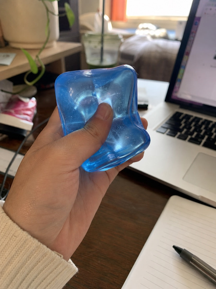 A hand squeezing a blue squishy toy beside a laptop and notebook