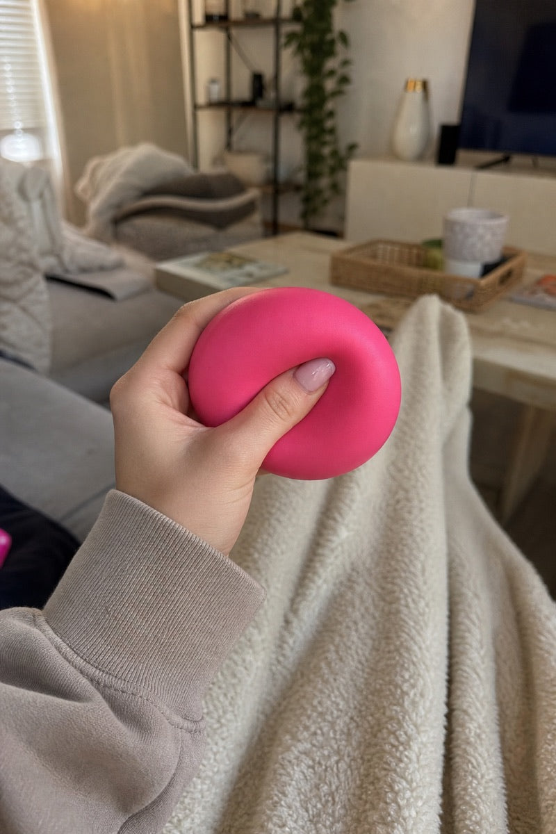 A hand squeezing a pink squishy toy while relaxing on a sofa